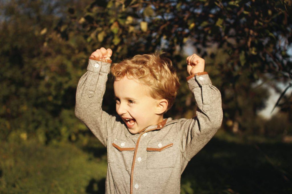 Child smiling and raising their arms above their head with excitement